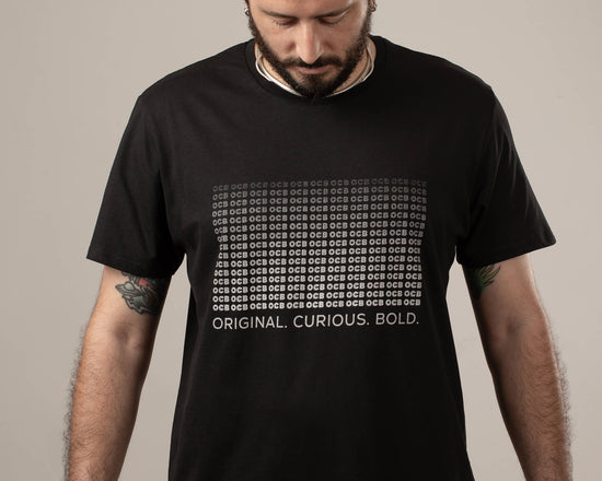 A person wearing a black OCB t-shirt with white text that reads 'ORIGINAL, CURIOUS, BOLD.'